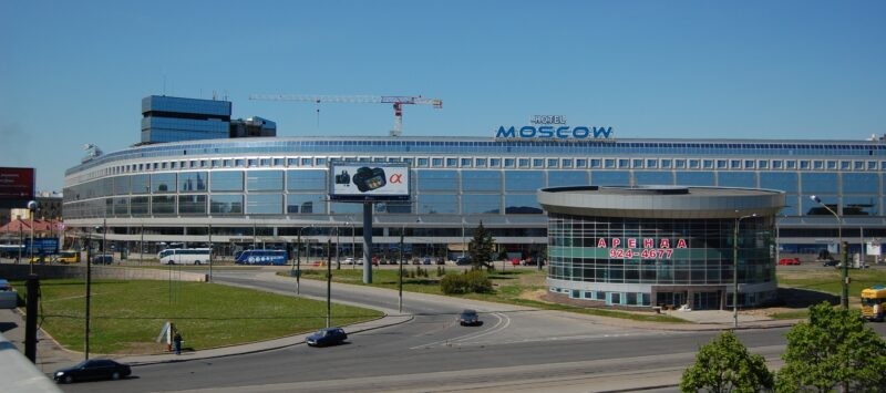Современное здание гостиницы "Москва" с зеркальным фасадом и рекламным щитом на переднем плане, вид с улицы при ярком солнечном дне.